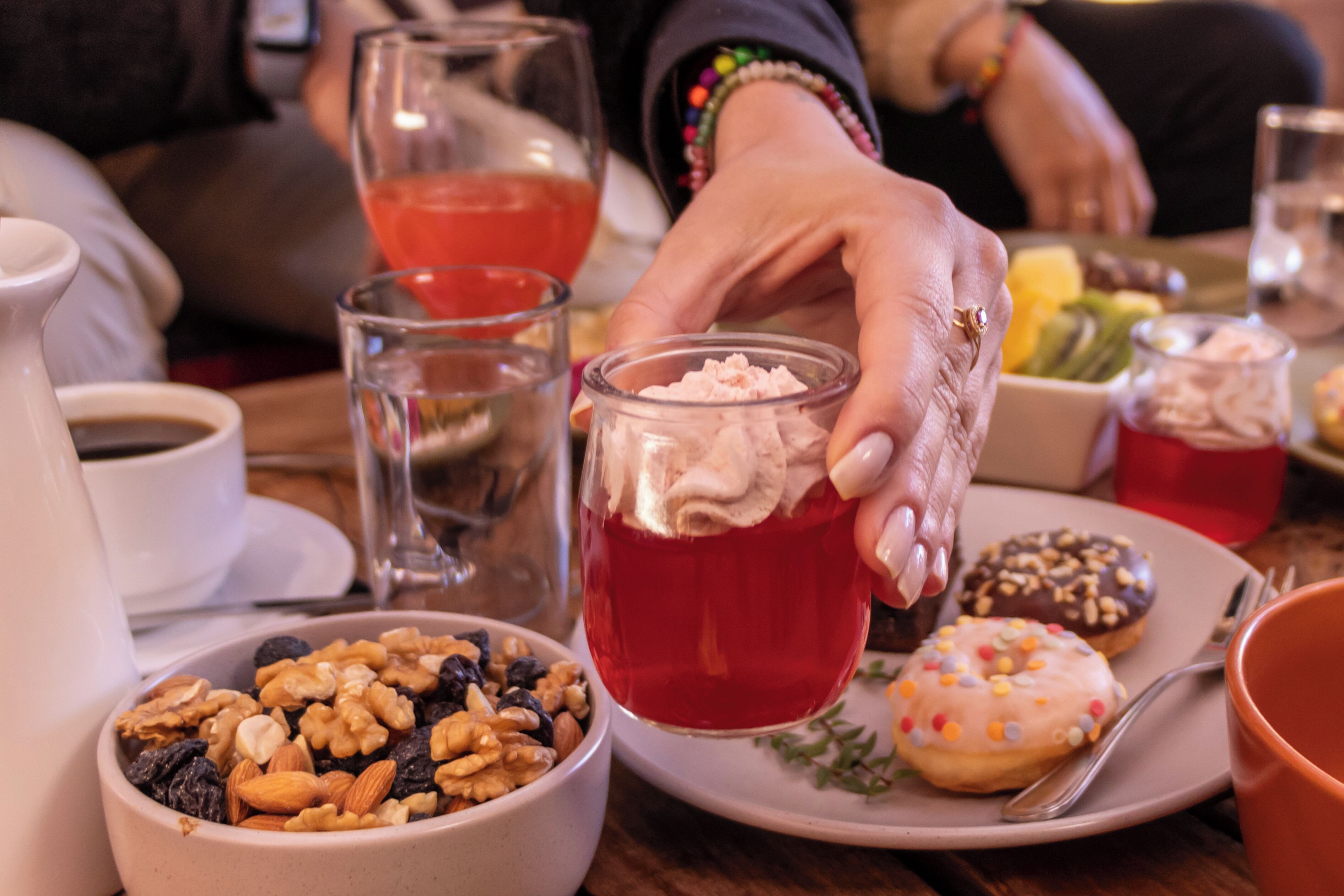 A dining table with various food items, including a bowl of nuts, a plate with donuts, and a glass of red beverage.