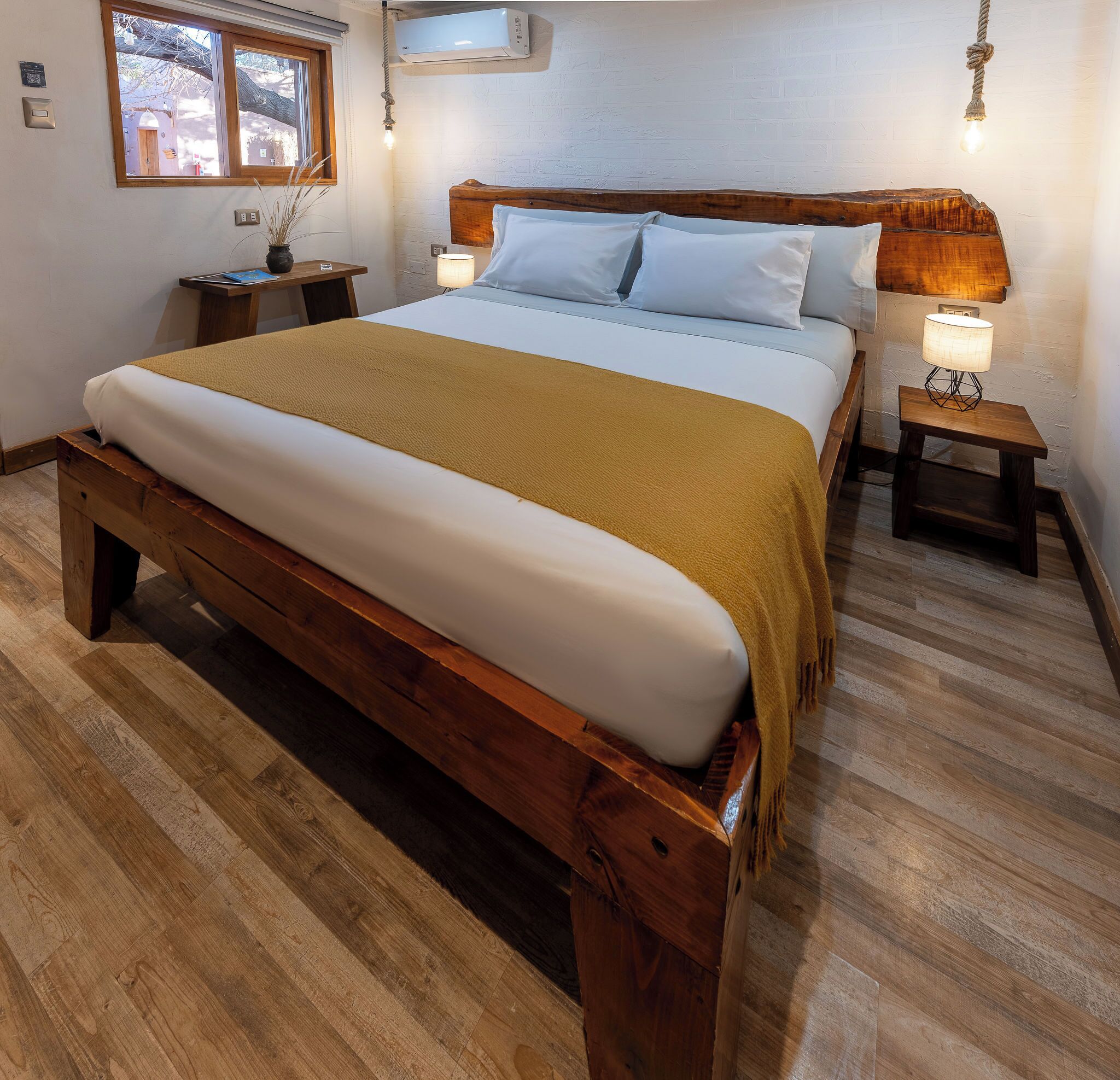 A bedroom with a wooden bed frame, white bedding, a mustard-colored throw, and two bedside lamps.