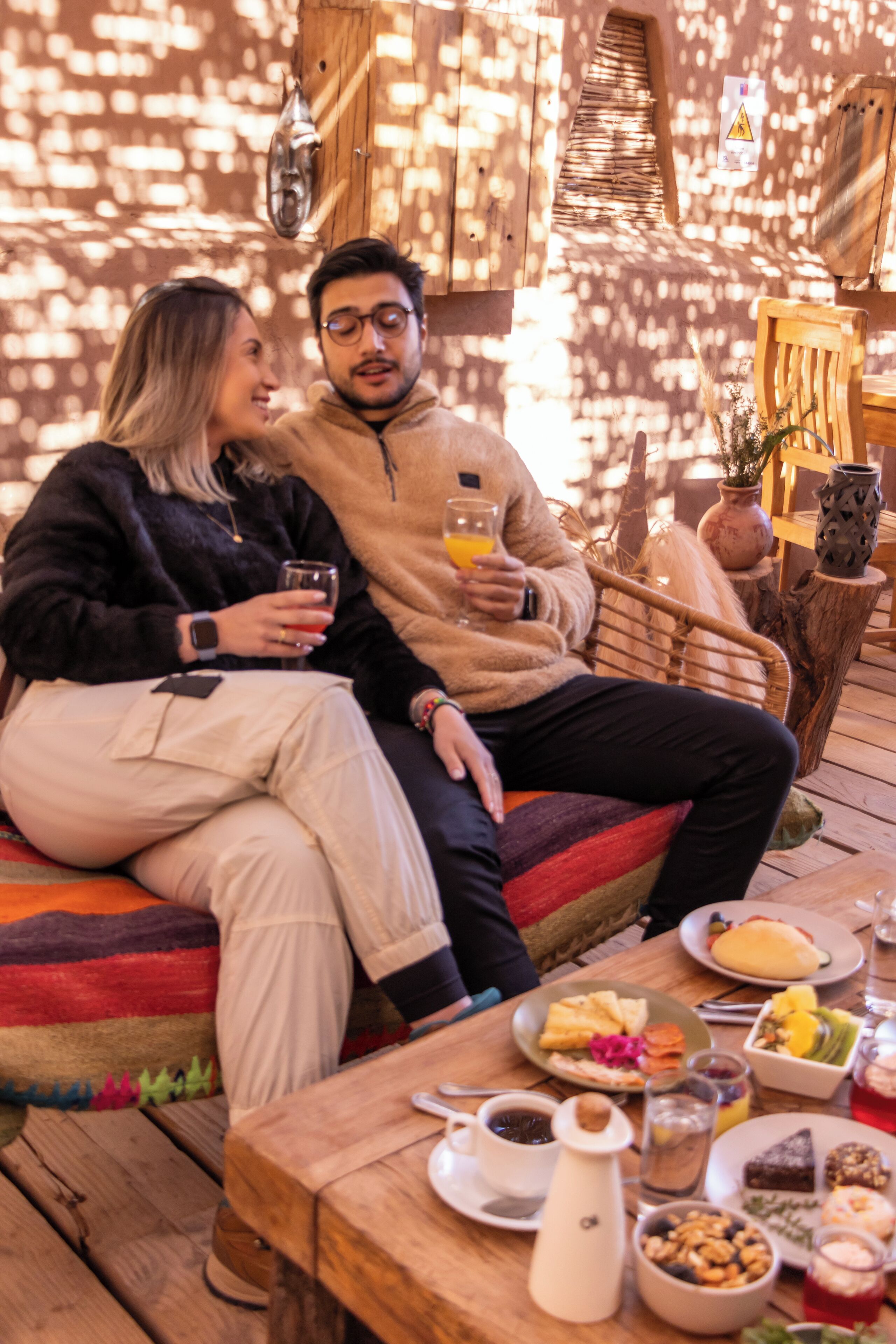 Una pareja sentada en un banco de madera frente a una mesa llena de comida y bebidas.