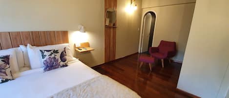 A bedroom with a bed, a nightstand with a lamp, a red chair, and a wooden ceiling.