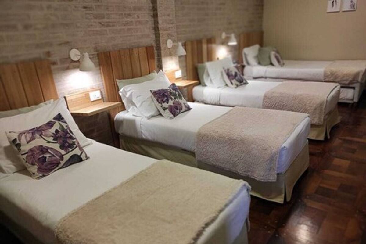 A room with three single beds, each with a wooden headboard, white bedding, and a floral pillow. There are bedside lamps on wooden nightstands.