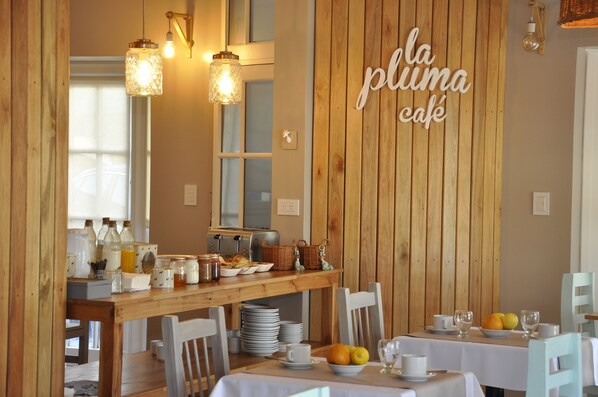 A breakfast setup with a wooden table, white chairs, and a sign that reads "la pluma café".