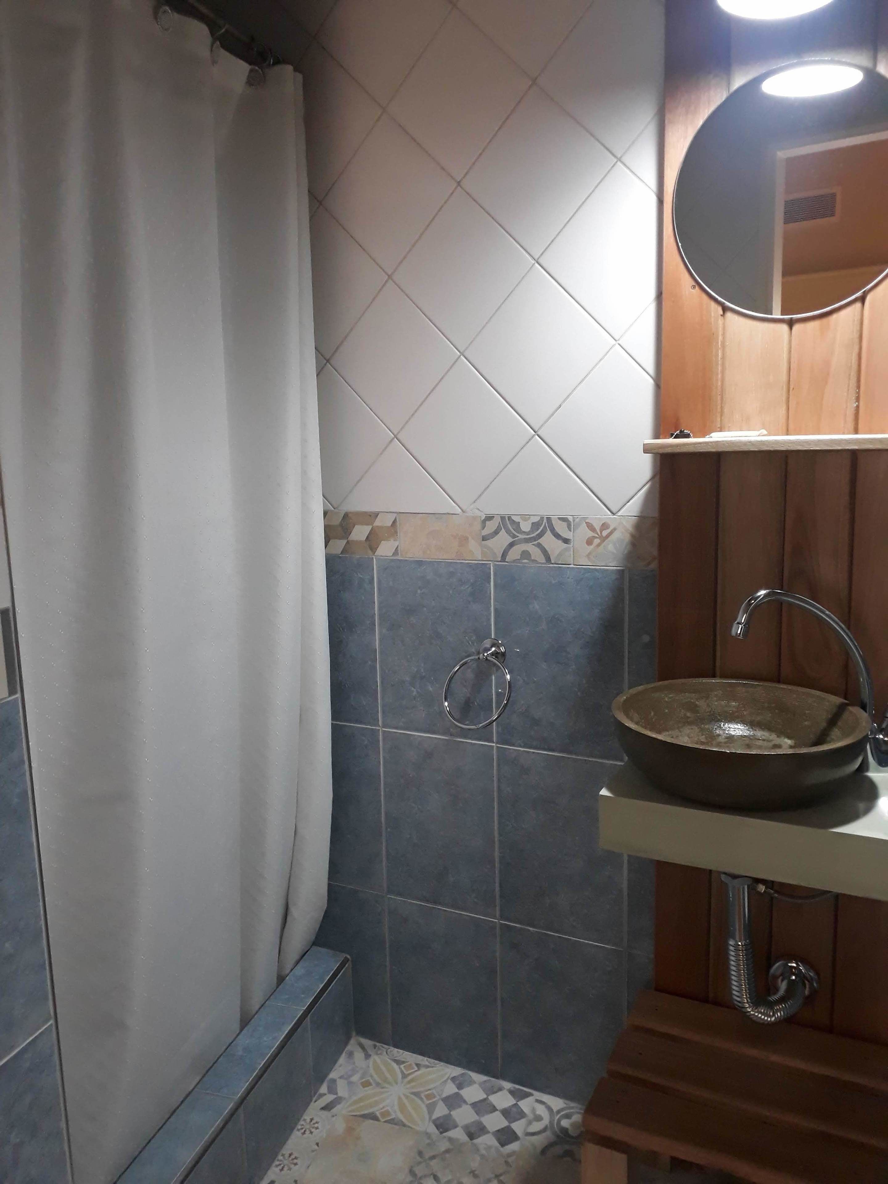 A bathroom with a shower curtain, a sink with a mirror above it, and tiled walls.