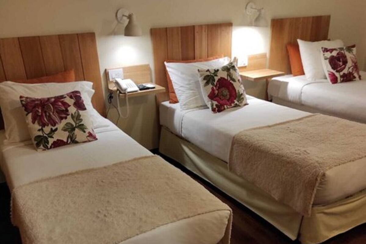 A hotel room with two beds, wooden headboards, bedside lamps, and floral-patterned pillows.