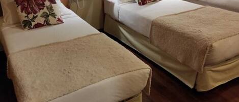 A hotel room with two beds, wooden headboards, bedside lamps, and floral-patterned pillows.