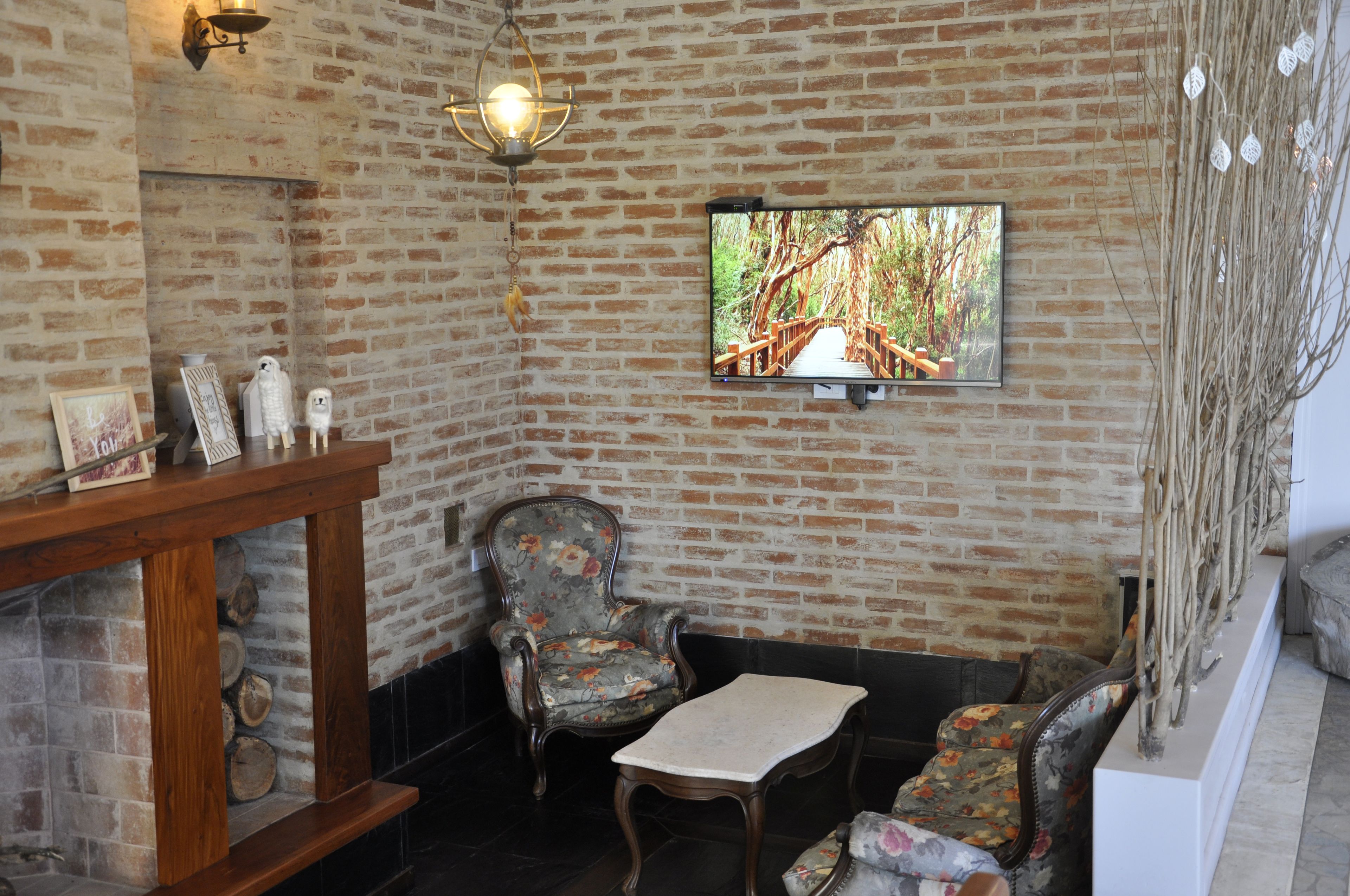 A cozy room with a brick wall, a wooden table, two chairs, a television, and a fireplace.