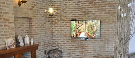 A cozy room with a brick wall, a wooden table, two chairs, a television, and a fireplace.