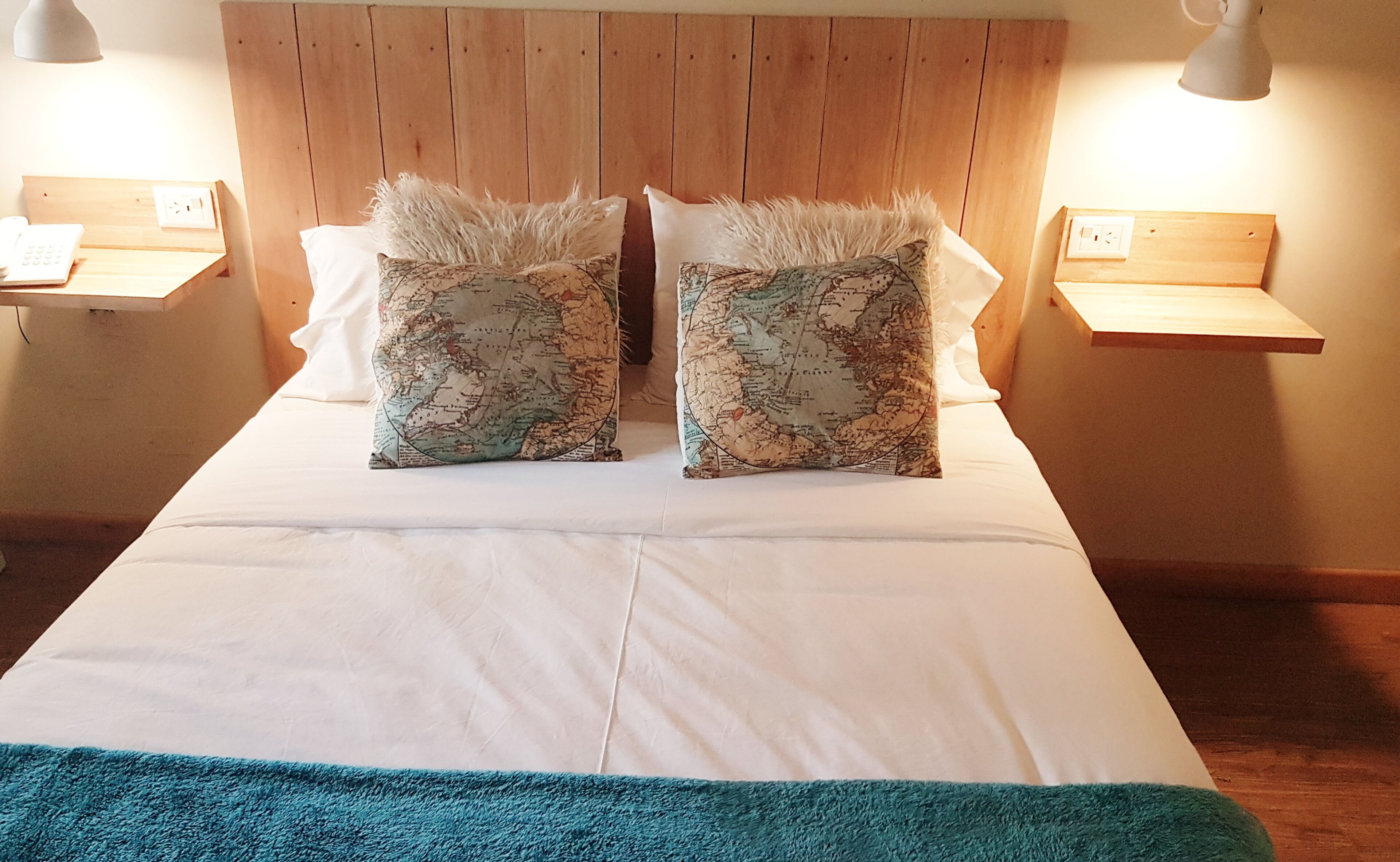 Un lit avec une literie blanche, deux coussins décoratifs ornés d’un motif de carte et une tête de lit en bois.