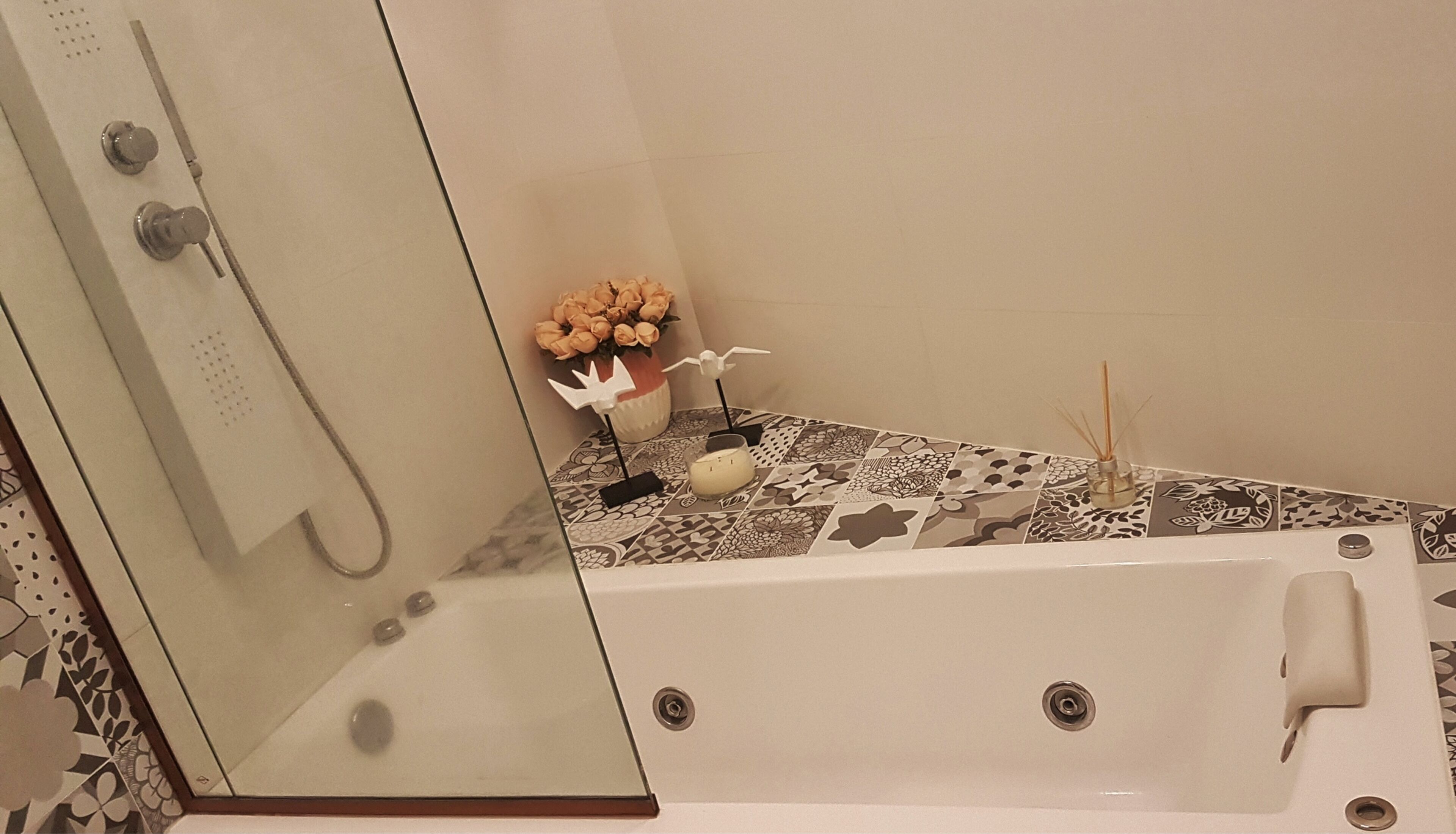 A bathroom with a glass-enclosed shower, a bathtub, and a decorative table with flowers and a candle.
