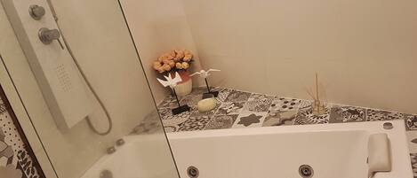 A bathroom with a glass-enclosed shower, a bathtub, and a decorative table with flowers and a candle.