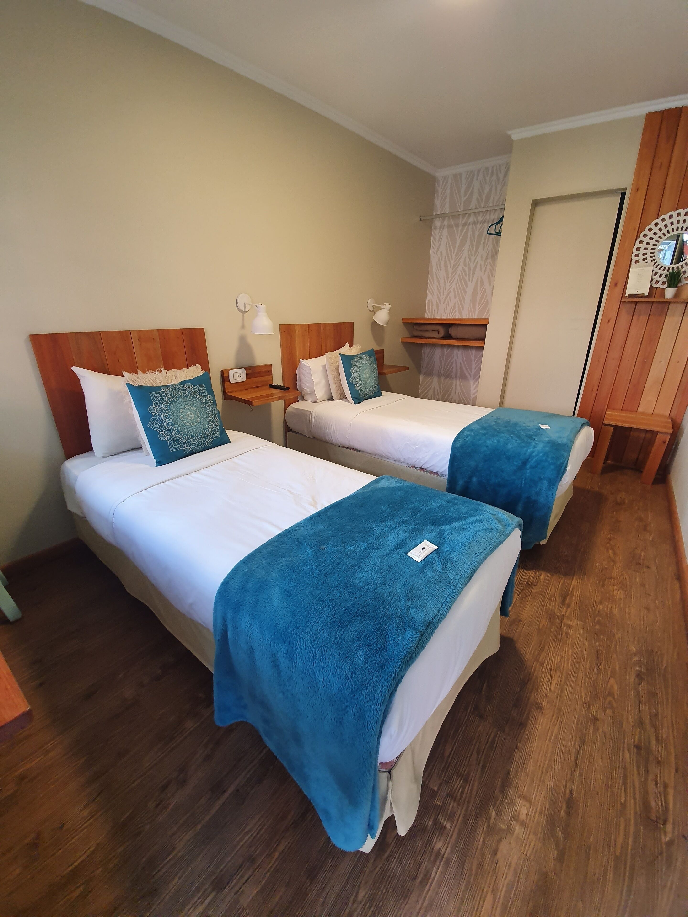 Habitación de hotel con dos camas, cabeceros de madera, ropa de cama blanca y mantas azules.
