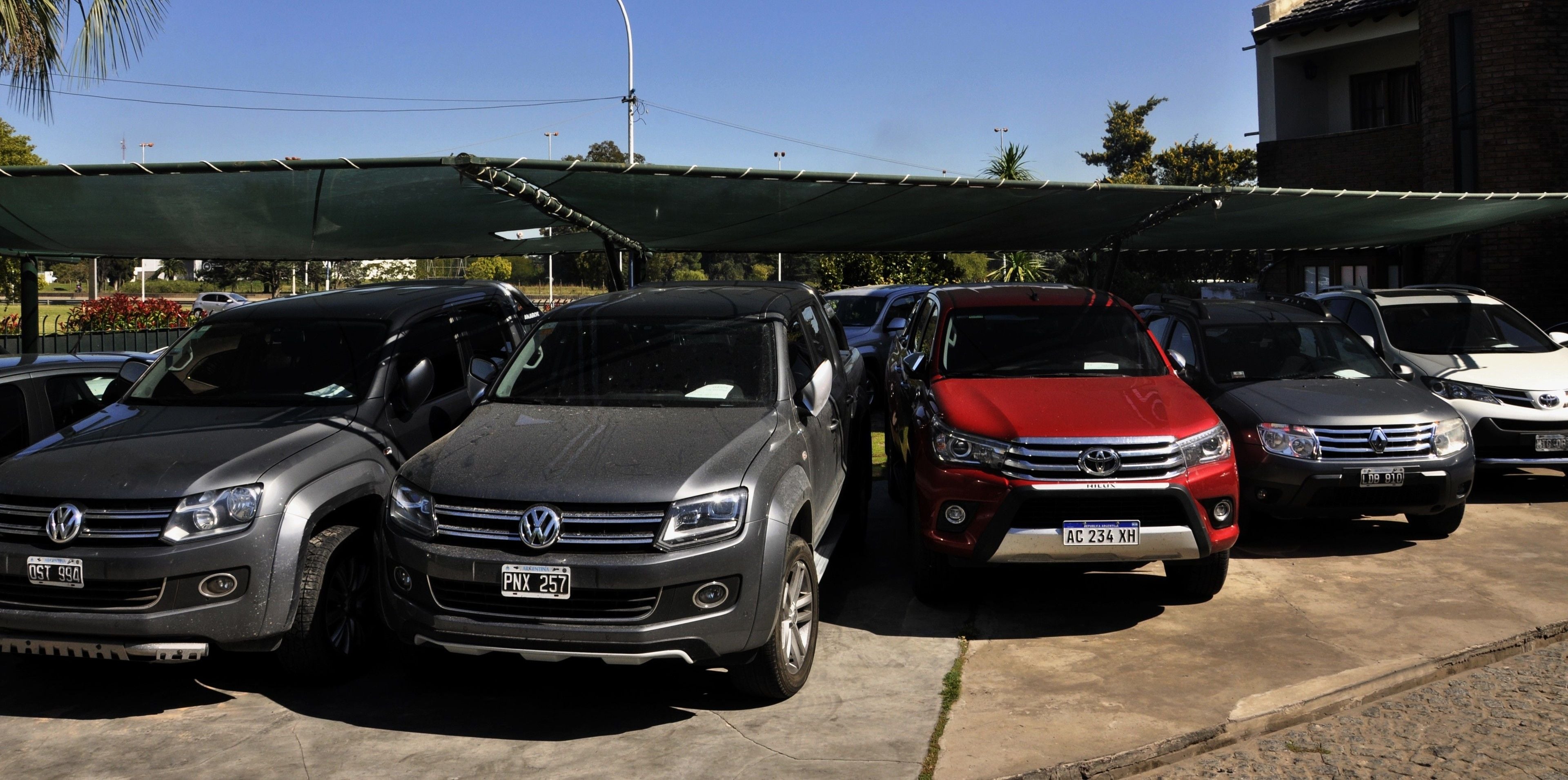 A parking lot with several cars, including a red and a silver SUV, under a green canopy.