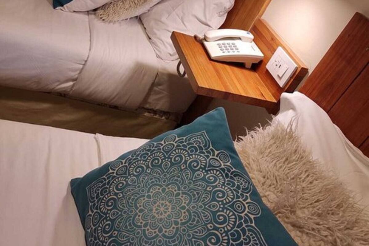 A hotel room with two beds, a wooden nightstand with a telephone, and a decorative pillow.