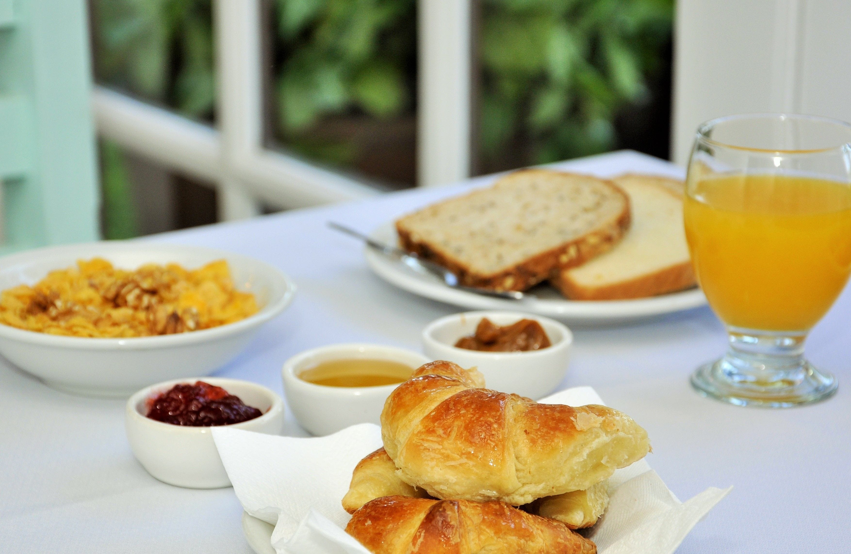 A breakfast table with croissants, toast, fruit compote, and orange juice.