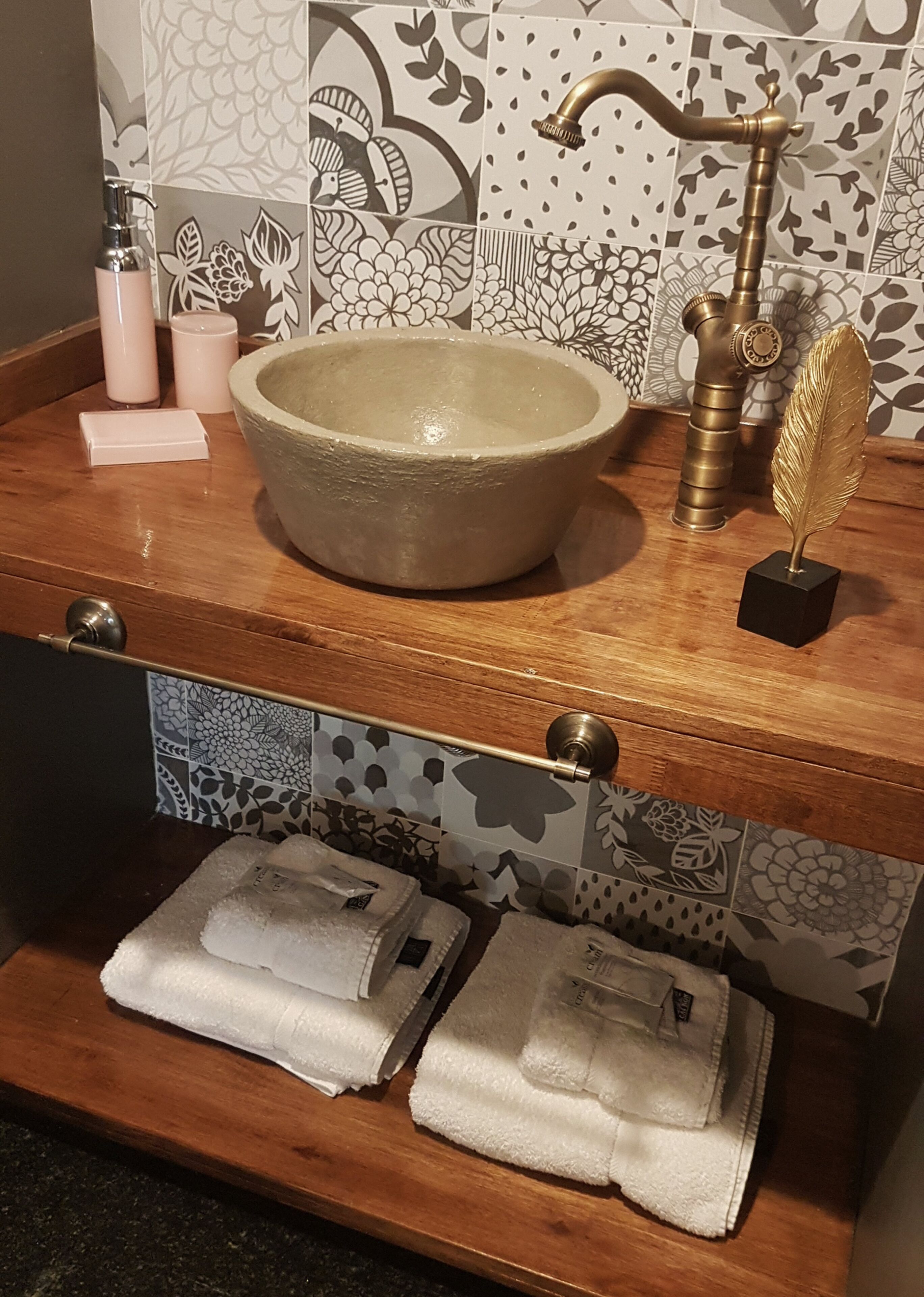 Une salle de bain avec un grand lavabo en céramique, un robinet doré et une plume décorative. Il y a deux serviettes sur le comptoir et un porte-savon.