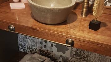 Un baño con un lavamanos de cerámica grande, un grifo dorado y una pluma decorativa. Hay dos toallas en la encimera y un jabonera.