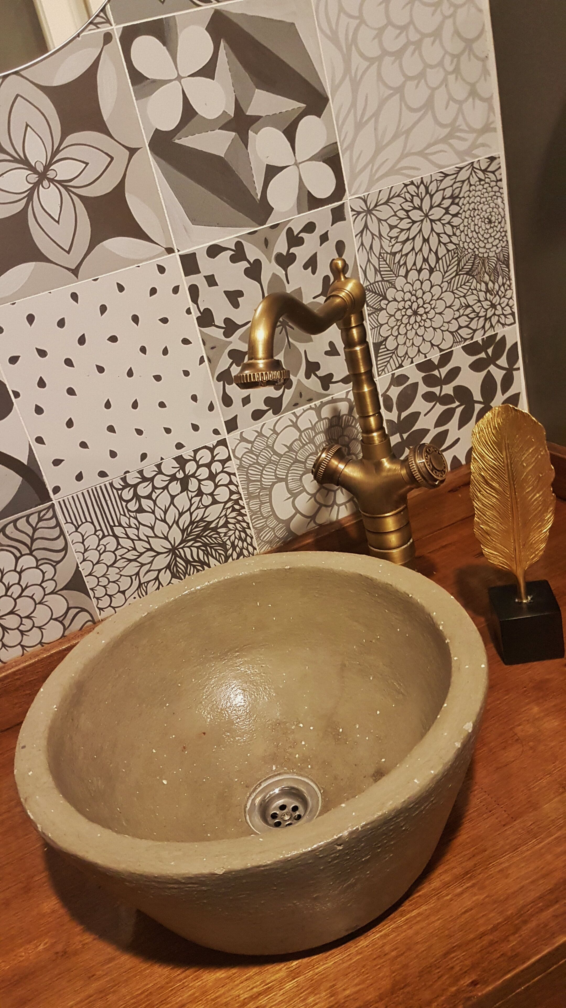 A bathroom sink with a gold faucet, a decorative feather, and patterned tiles in the background.
