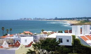 A coastal residential area with houses, a beach, and a distant city skyline. - Hostal de la Barra (Punta del Este)