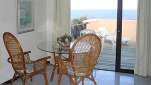 A room with a glass table and wicker chairs, a framed picture on the wall, and a view of the beach through a sliding door. - Hostal de la Barra (Punta del Este)