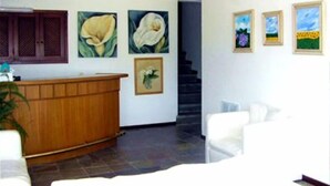 A reception area with a wooden desk, a staircase, and several framed artworks on the walls. - Hostal de la Barra (Punta del Este)