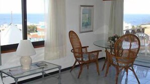 A room with a glass table, wicker chairs, a white lamp, and a view of the sea through large windows. - Hostal de la Barra (Punta del Este)