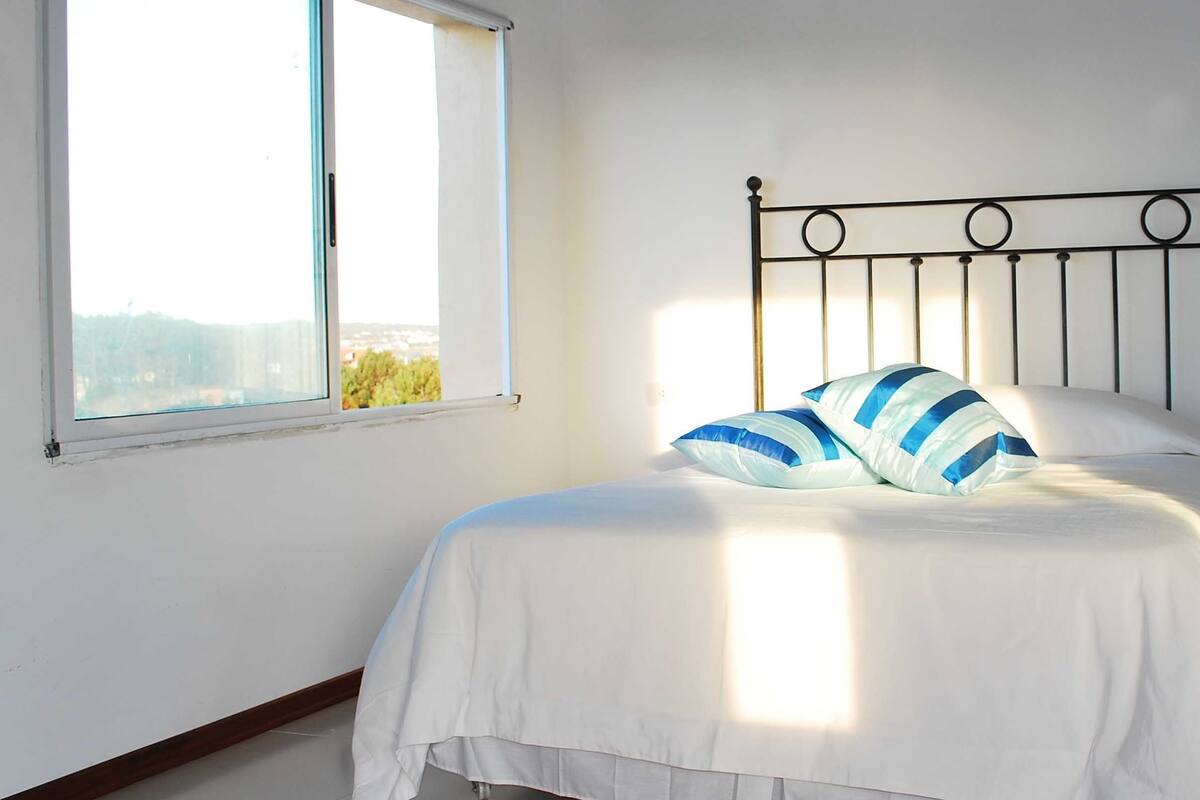 A single bed with a metal headboard, white bedding, and a striped pillow.
