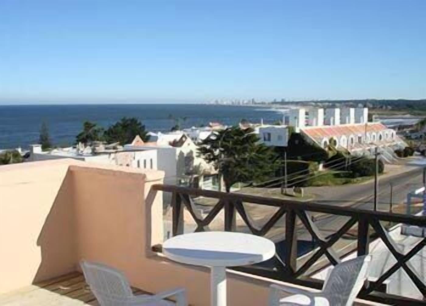 A balcony with a table and chairs overlooking a coastal cityscape.