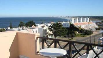 A balcony with a table and chairs overlooking a coastal cityscape.