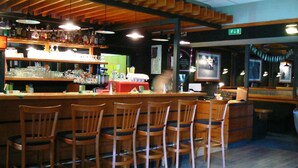 Un espace bar avec des chaises en bois, un comptoir où sont exposées différentes bouteilles et un écran de télévision.