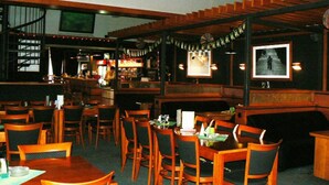 Un restaurant avec des banquettes et des tables en bois, un bar et un escalier.
