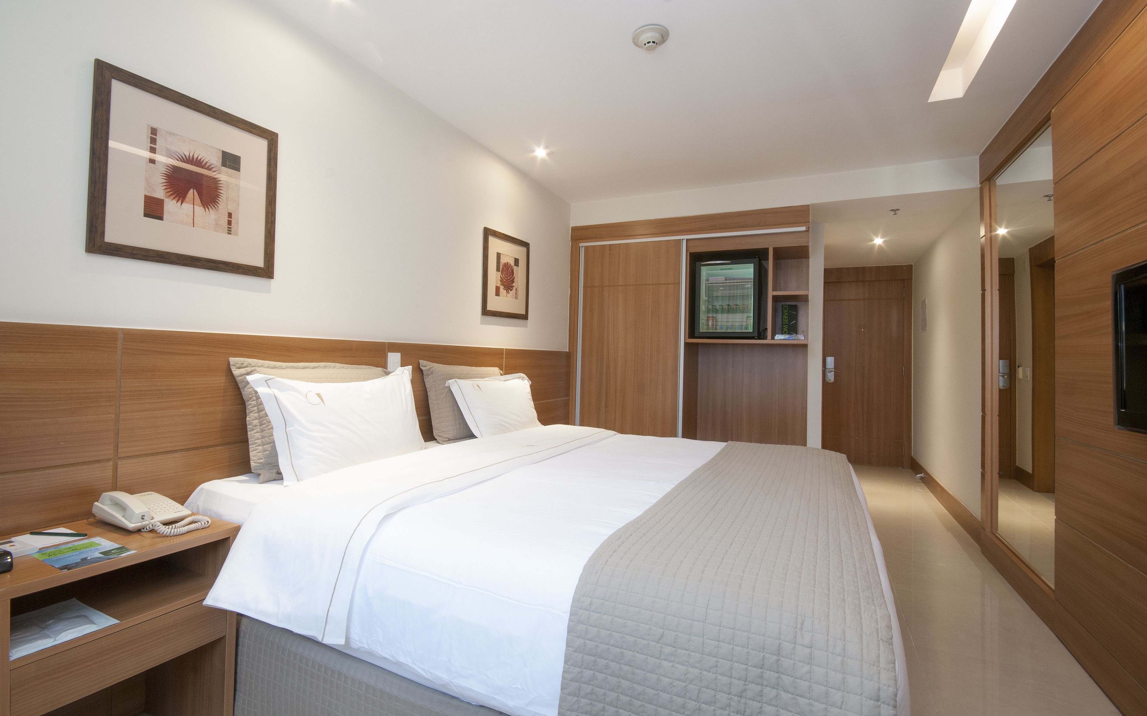 A hotel room with a large bed, bedside tables, a desk with a phone, a TV, and a wardrobe.