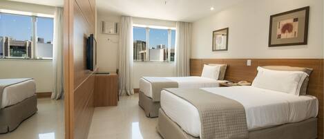 Habitación de hotel con dos camas, televisión, escritorio y ventana con vistas a la ciudad.
