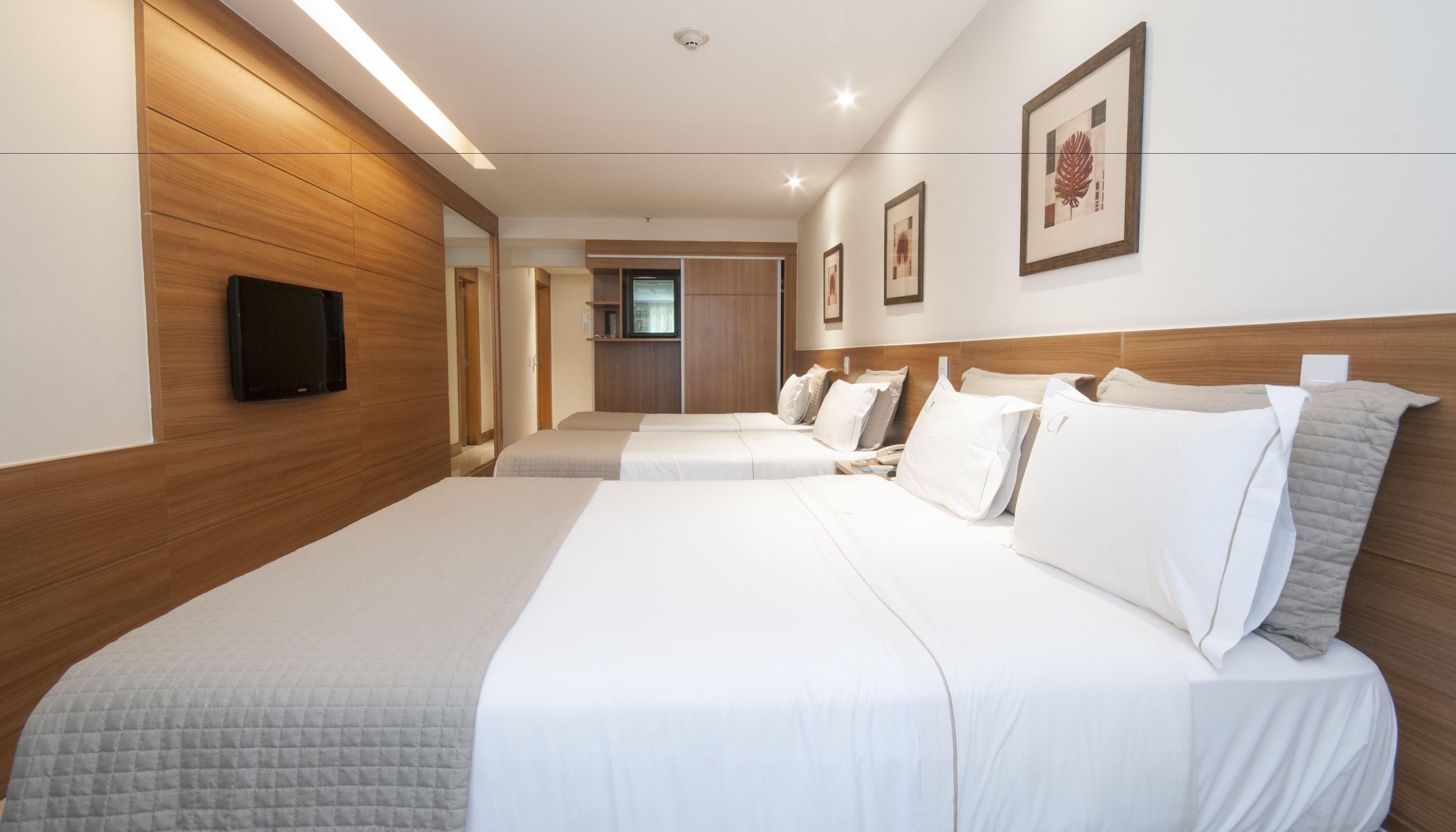 Habitación de hotel con dos camas, paneles de madera en las paredes, un televisor de pantalla plana montado en la pared y obras de arte enmarcadas.