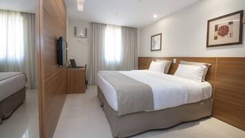 Quarto de hotel com cama, escrivaninha com laptop, televisão e quadro pendurado na parede.