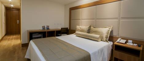 A hotel room with a bed, a desk, a chair, a minibar, and a telephone.