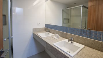 Un baño con dos lavamanos, una cabina de ducha de vidrio y un espejo que refleja un revestimiento de azulejos azules.