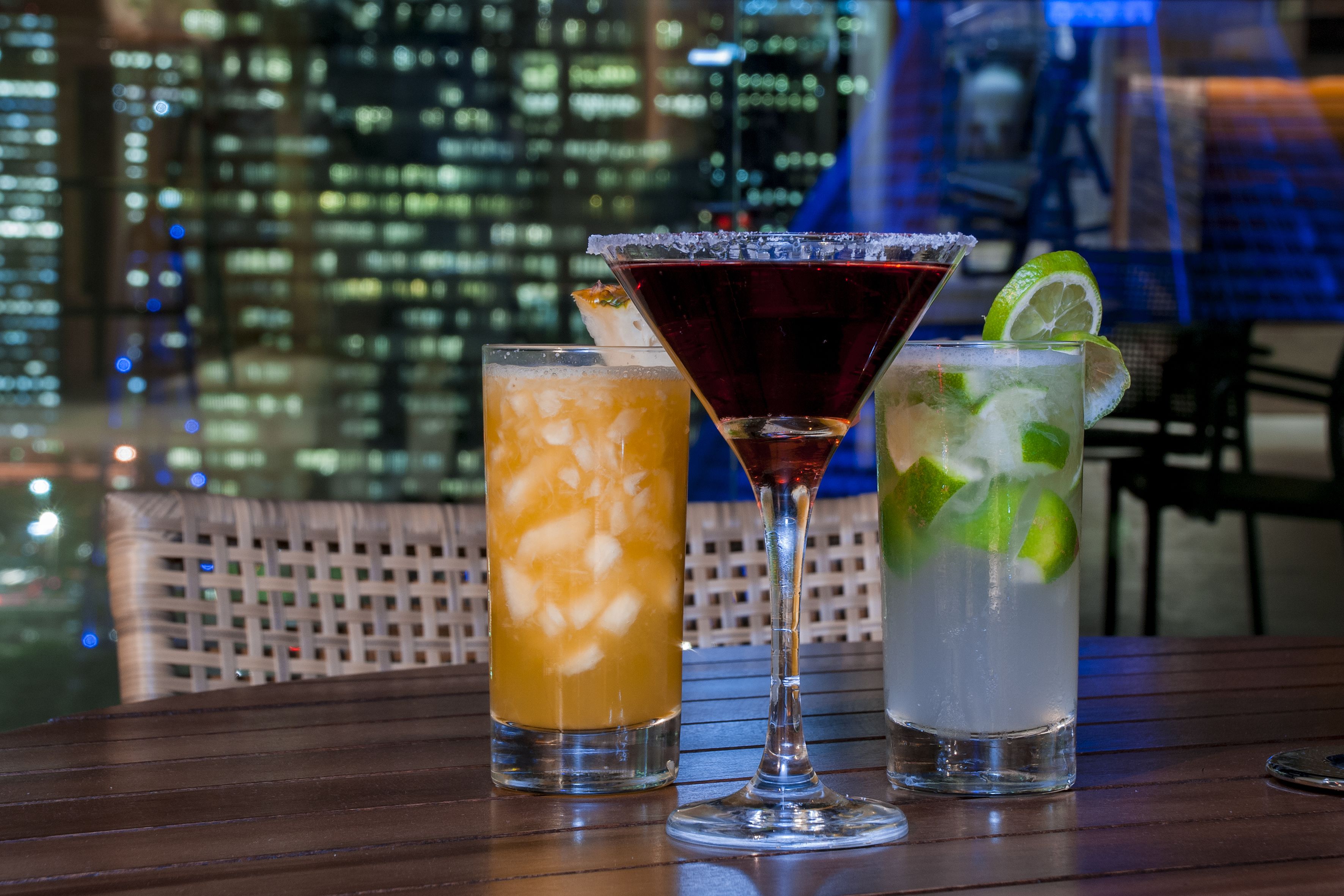 Three drinks on a table with a cityscape view in the background.