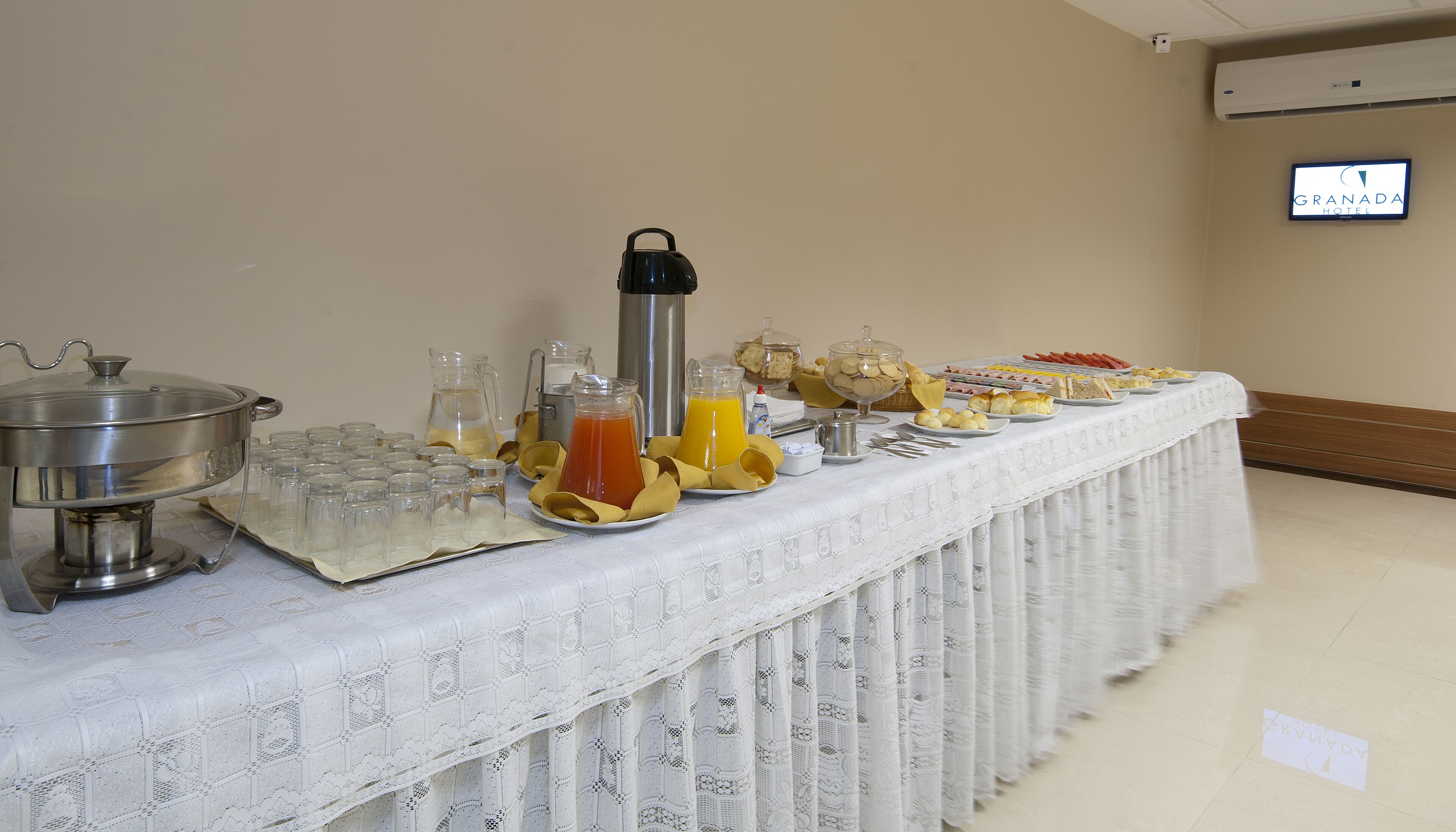 Een buffet tafel met diverse gerechten en drankjes, een koffiekan en een bordje met de naam van het hotel.