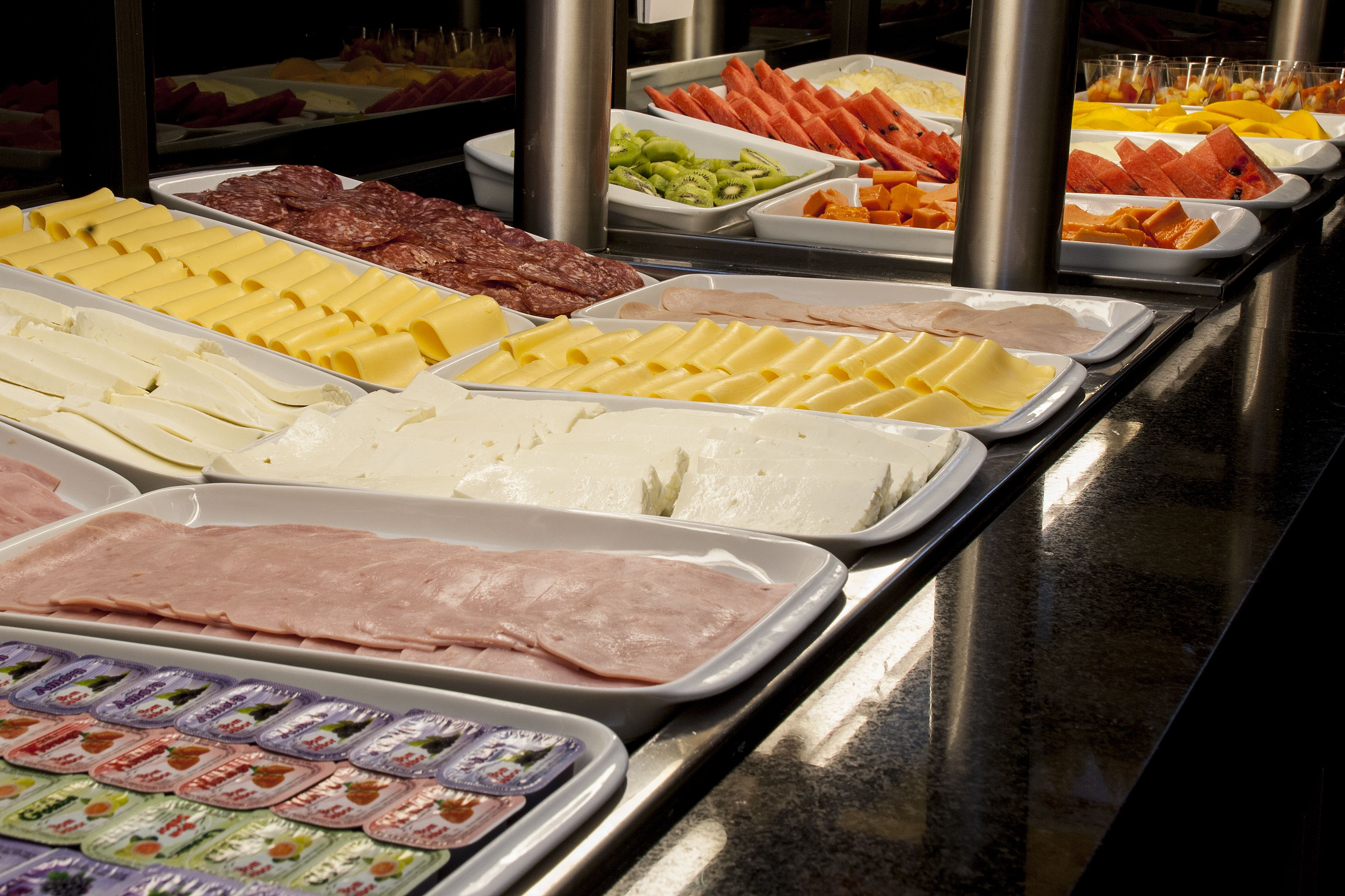 Buffet com diversos itens de comida, incluindo carnes, queijos e frutas.