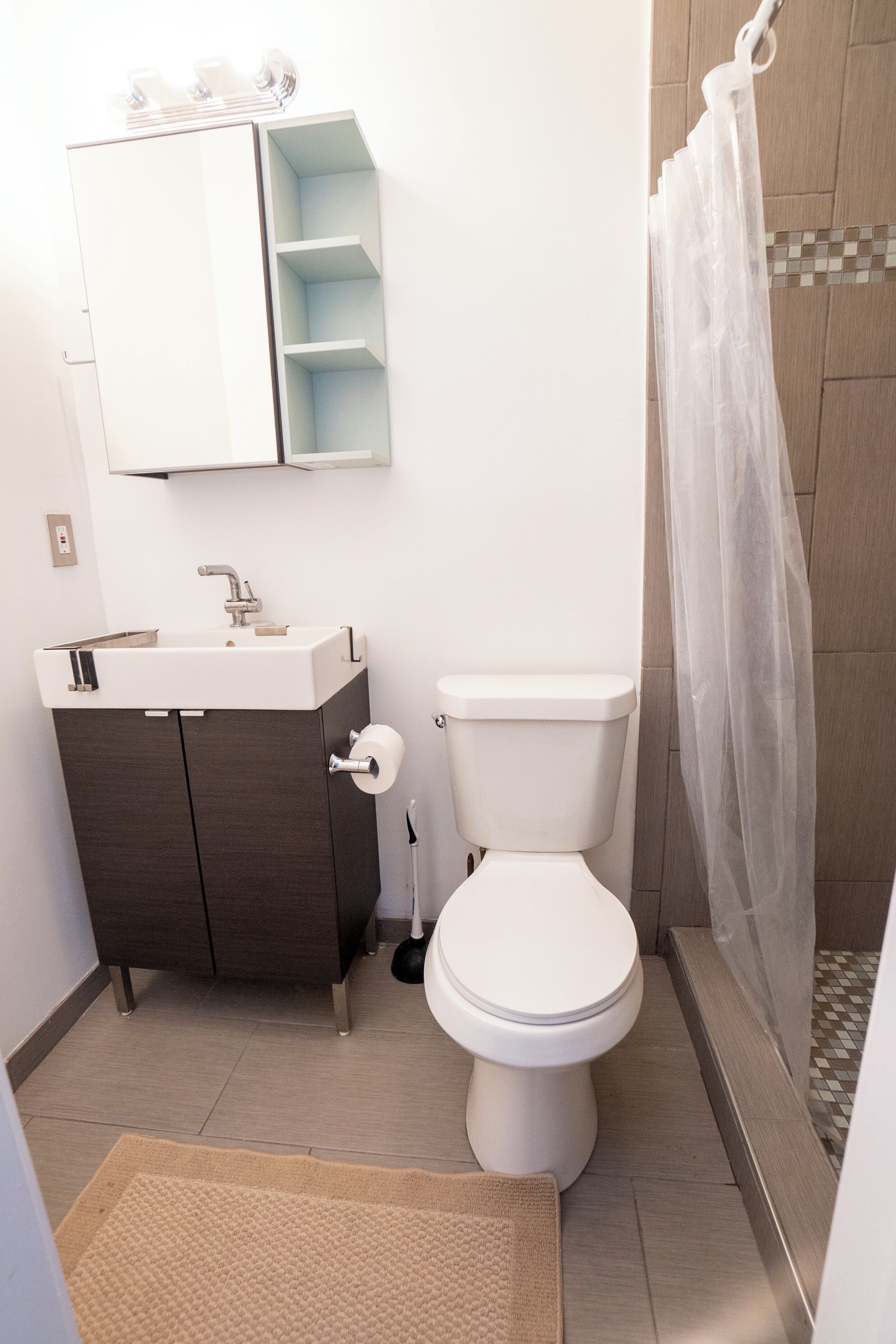 A bathroom with a white toilet, a dark wooden cabinet with a mirror, and a shower with a transparent curtain.