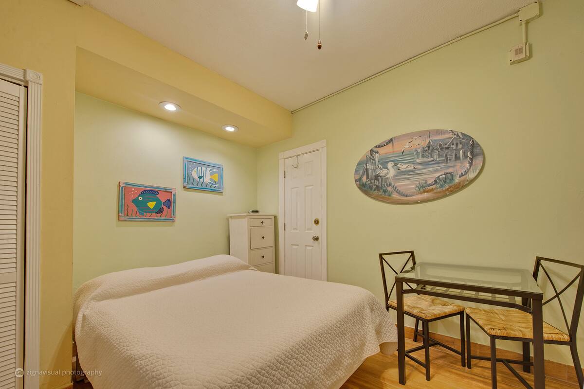 A bedroom with a bed, a dresser, a desk with two chairs, and wall art.