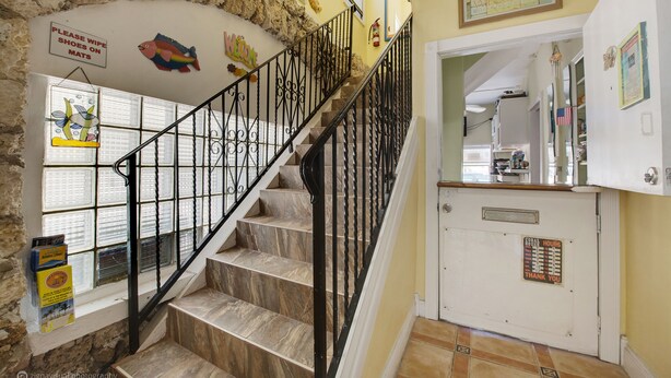 A staircase with black railings leading to a landing with a white door and a sign indicating 'CORAL HOUSE HOURS'. - The Coral House Motel (Hollywood)