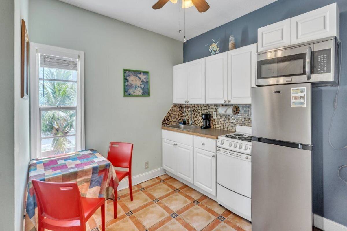 A compact kitchen with white cabinets, a microwave, a stove, and a ceiling fan.