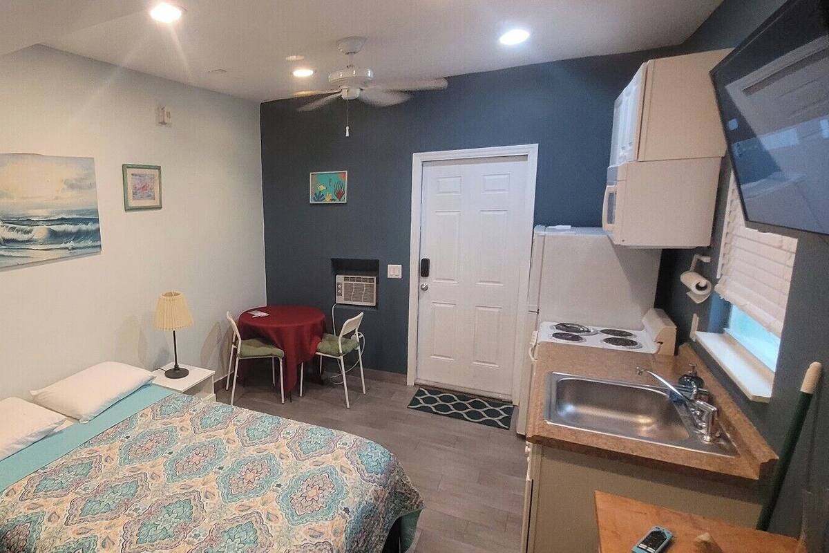 A compact room with a bed, a small dining table, a kitchenette, and a door leading to another room.