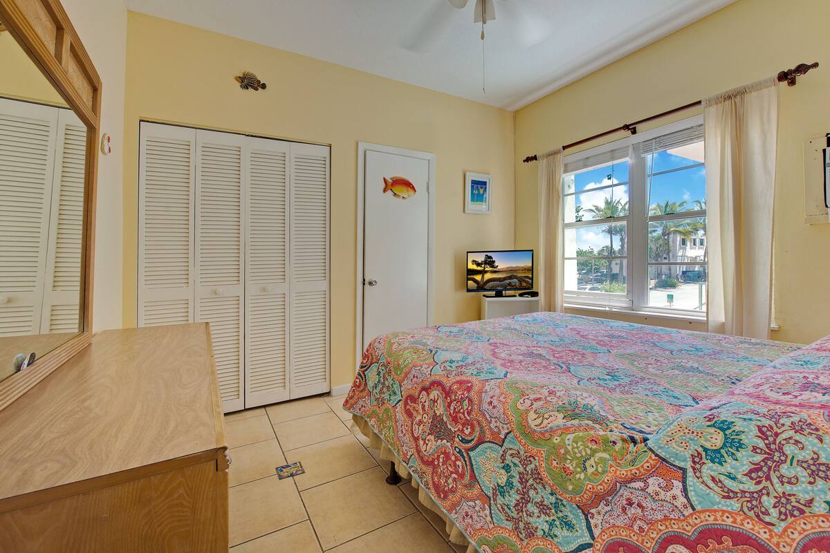 A bedroom with a large bed, a wooden dresser, a door with a fish decoration, and a window with curtains.