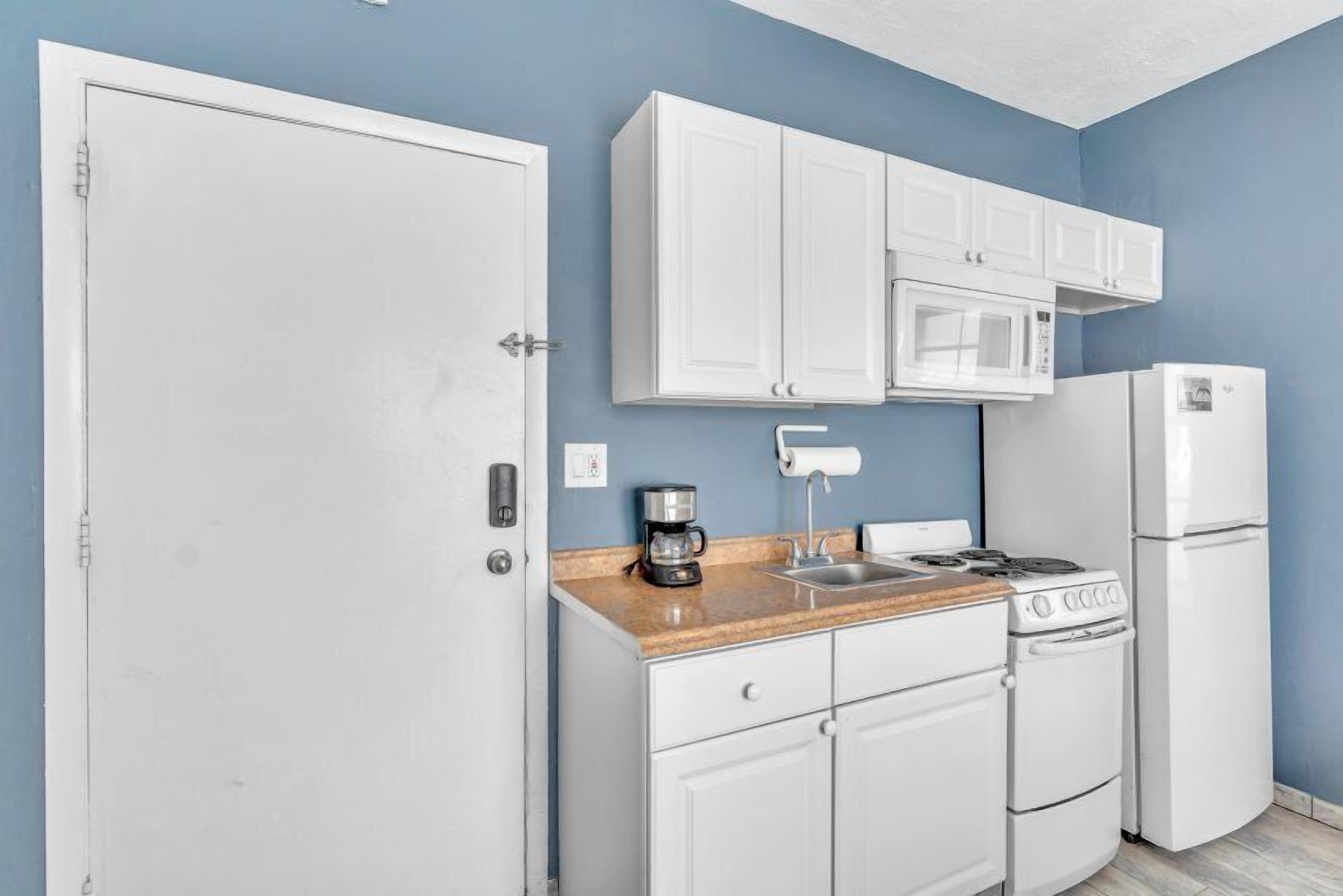 A compact kitchen with white cabinets, a microwave, a stove, and a refrigerator.