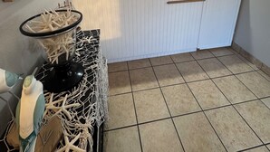 A kitchen with a tiled floor, a white cabinet, a glass container with sea shells, and a wall-mounted artwork.