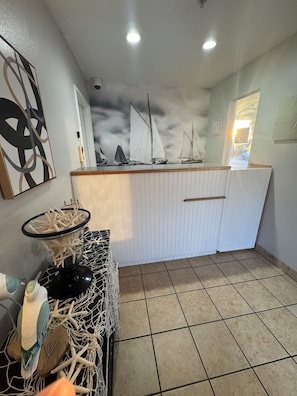 A kitchen with a tiled floor, a white cabinet, a glass container with sea shells, and a wall-mounted artwork.