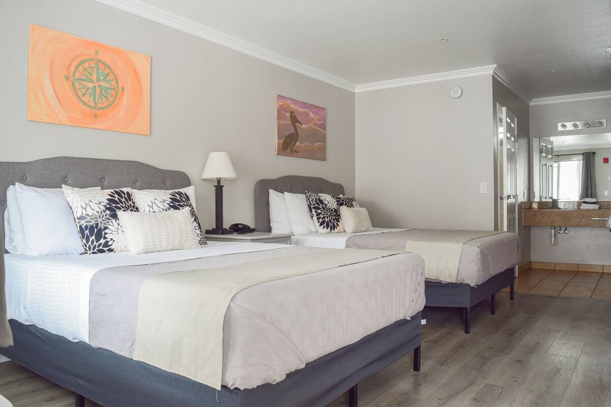 Ein Hotelzimmer mit zwei Betten, einem großen Spiegel, einem Waschbecken und einem Gemälde an der Wand.