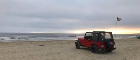 A red off-road vehicle parked on a sandy beach with an American flag on the back.